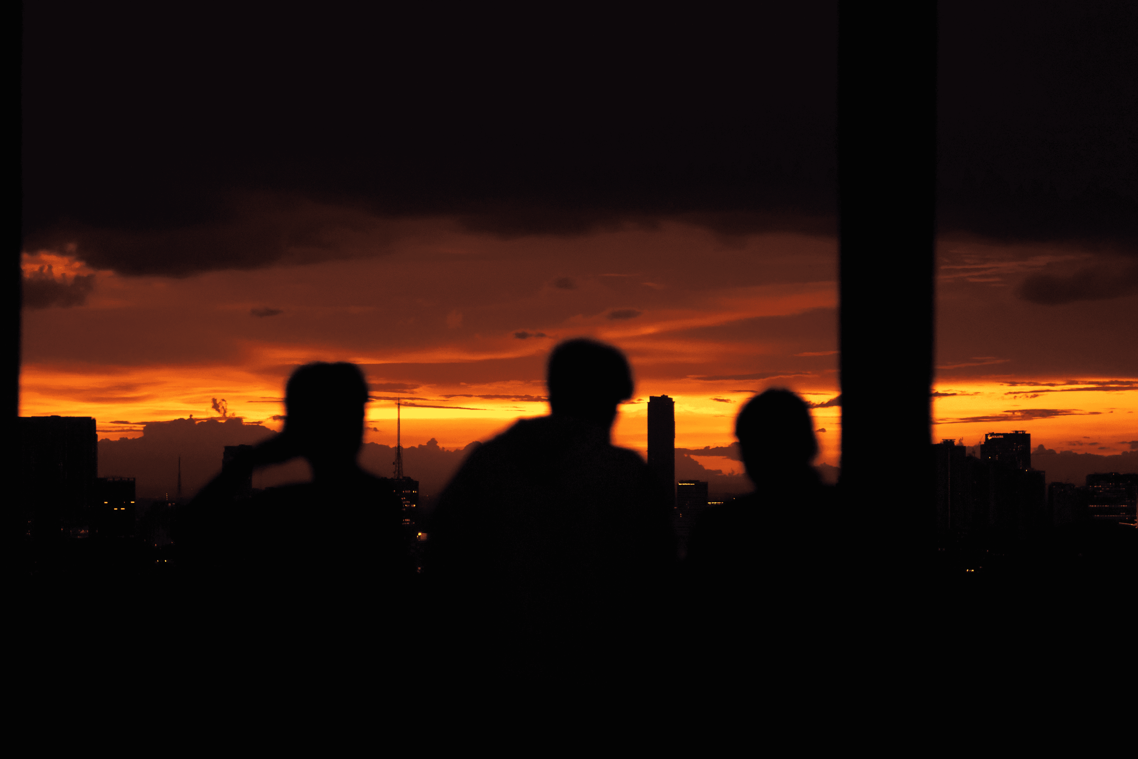 Three silhouettes against an orange sunset through a window